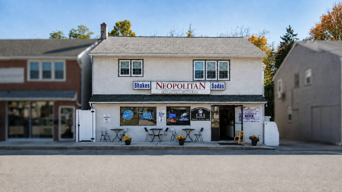The Neopolitan Delicatessen storefront on Lancaster Avenue — a white two-storey building with the red NEOPOLITAN sign and café tables out front